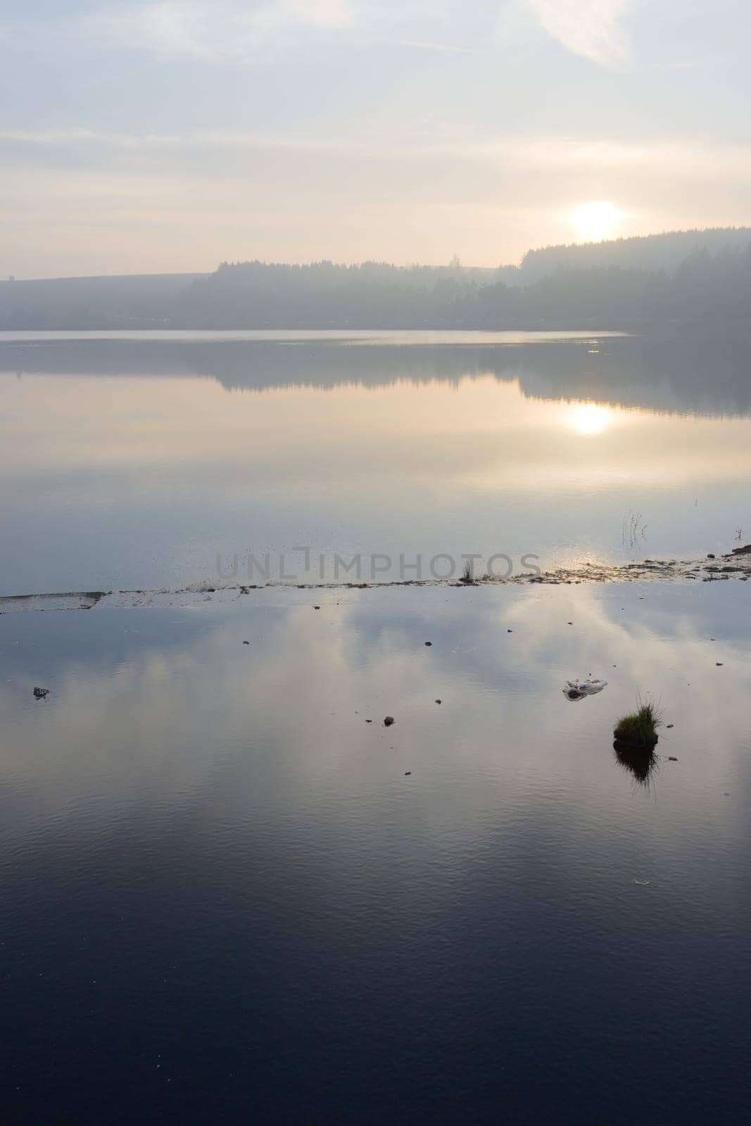 Misty landscape and wispy clouds reflected in calm reservoir water. Vertical sunset image over redmires reservoir, at the top reservoir.