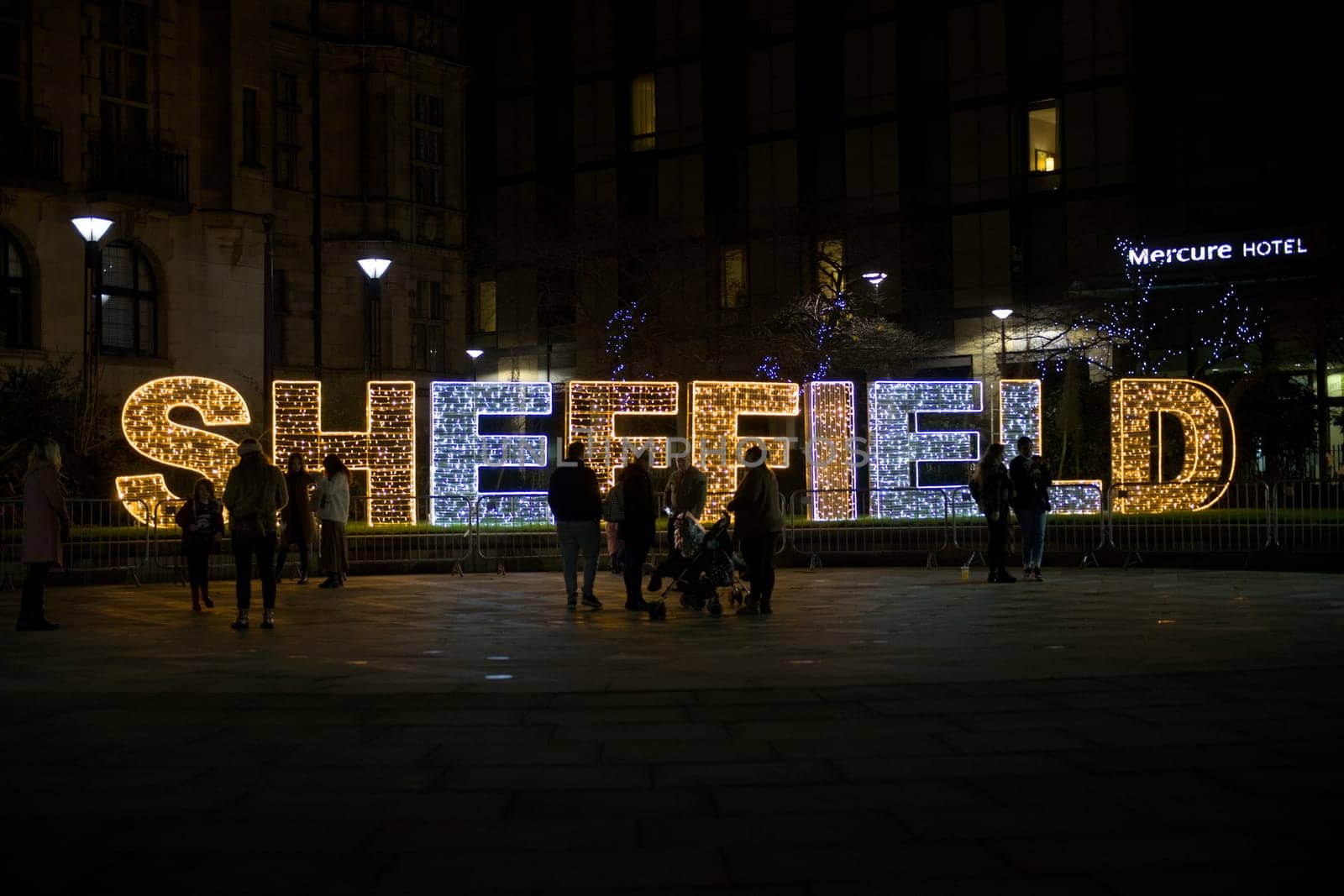 Sheffield, United Kingdom, 27th November, 2020: Close up of Sheffield illuminated with christmas fairy lights. groups of people stand in front.