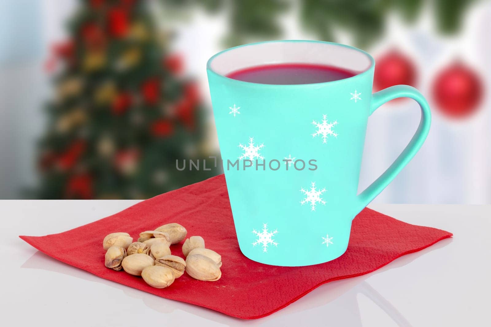 Christmas hot mulled wine or punch and pistachios on a red napkin on the table against a blurred Christmas background. Space.