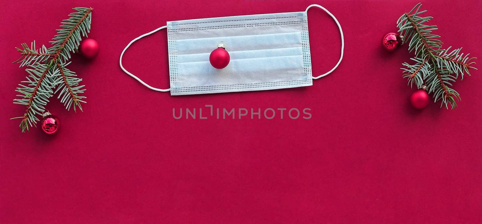 Corona and Christmas. A protective mask next to Christmas tree balls and fir branches on a pink background
