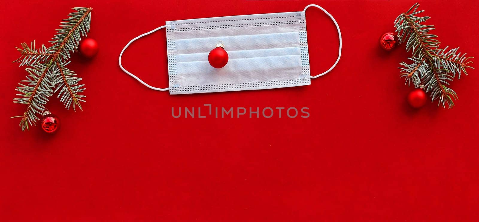 Corona and Christmas. A protective mask next to Christmas tree balls and fir branches on a red background