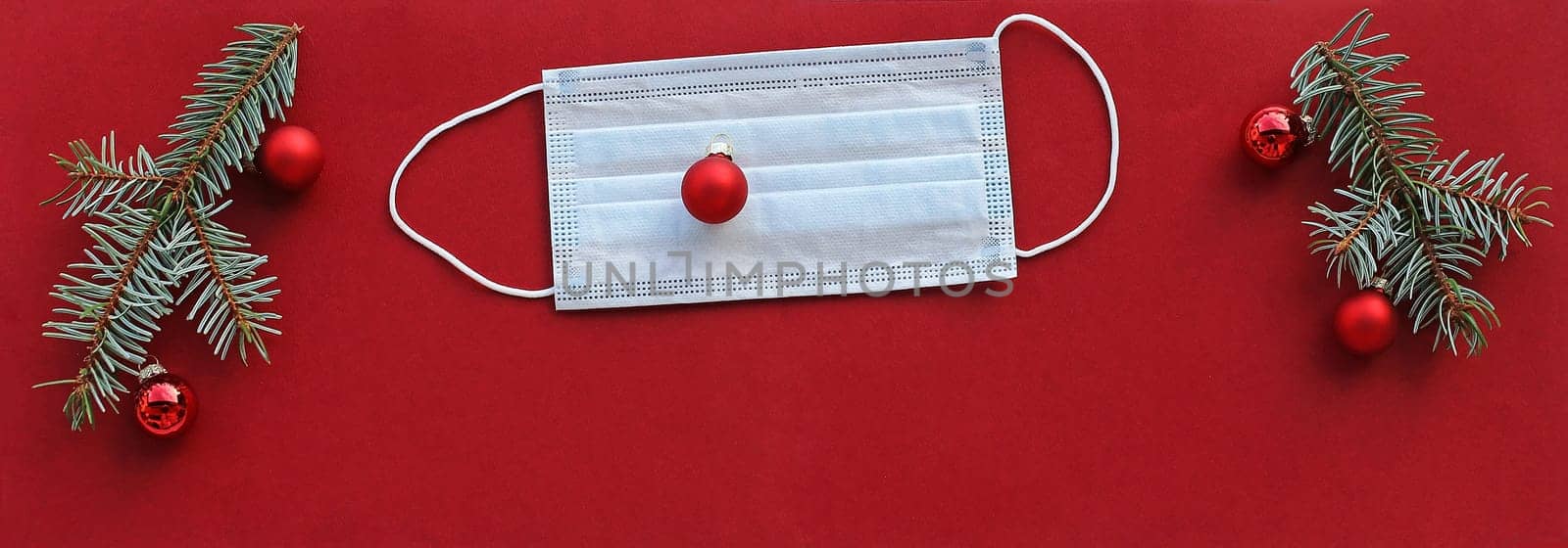 Corona and Christmas. A protective mask next to Christmas tree balls and fir branches on a red background