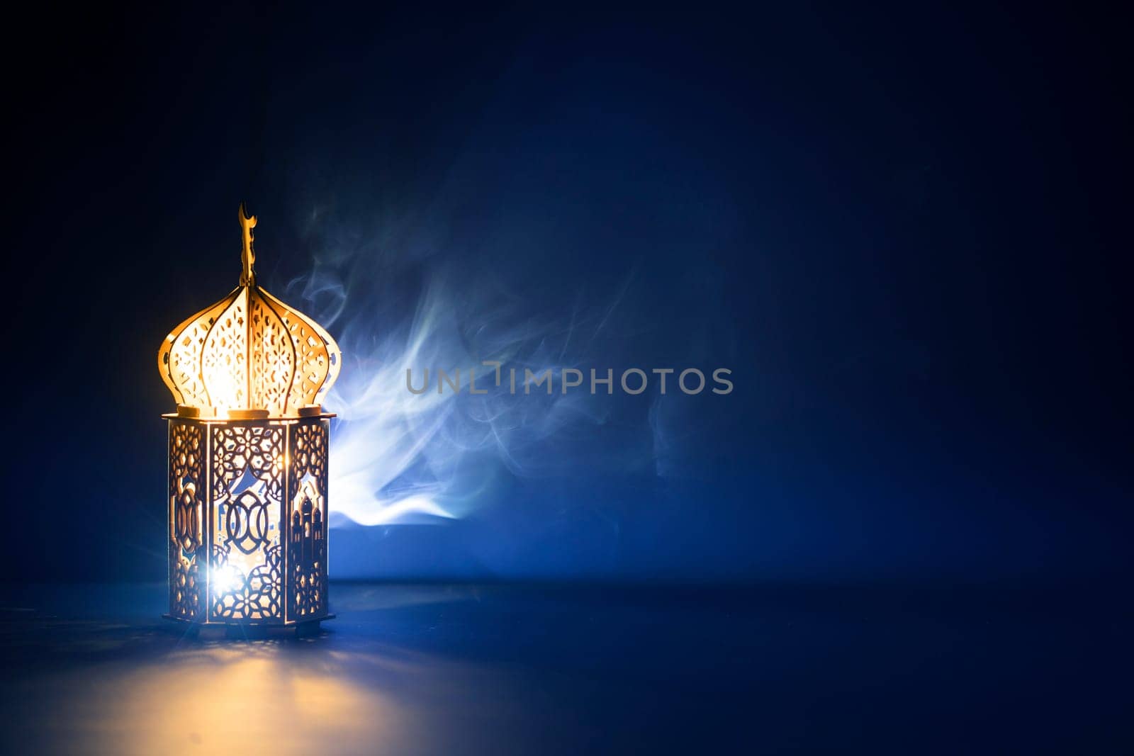 Ornamental Arabic lantern with burning candle glowing at night and glittering golden bokeh lights. Festive greeting card for Muslim holy month Ramadan Kareem.