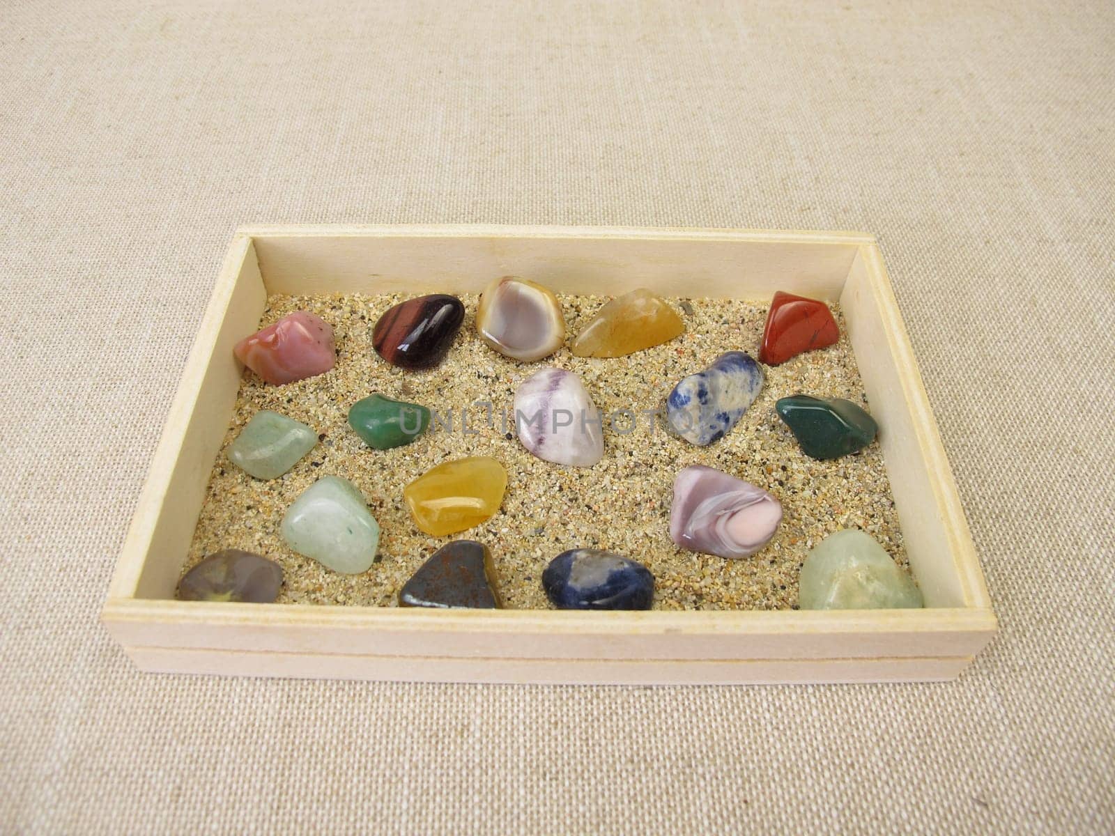 Tumbled gemstones in a wooden box with sand