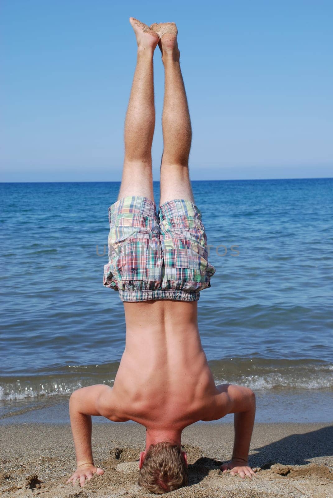 A sporty,muscular young man does a handstand on the beach.