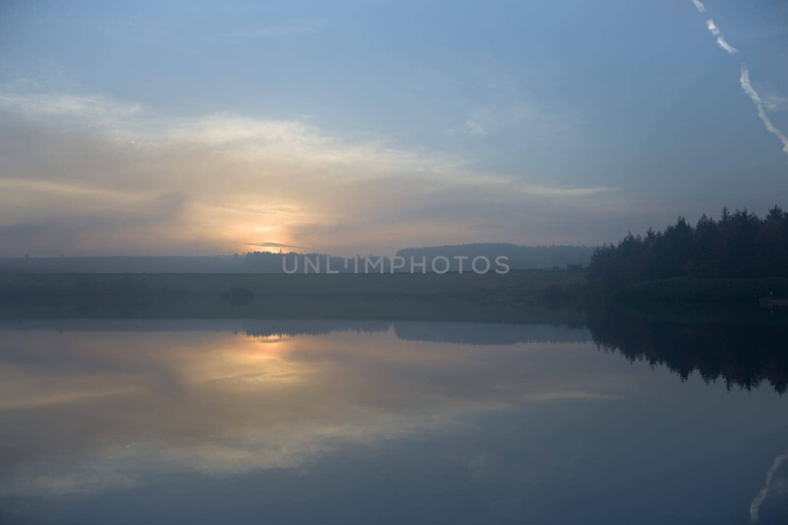Low clouds mask a misty sunset on the horizon. Taken at dusk over redmires reservoirs, the still water mirrors the sky and cloud scape.