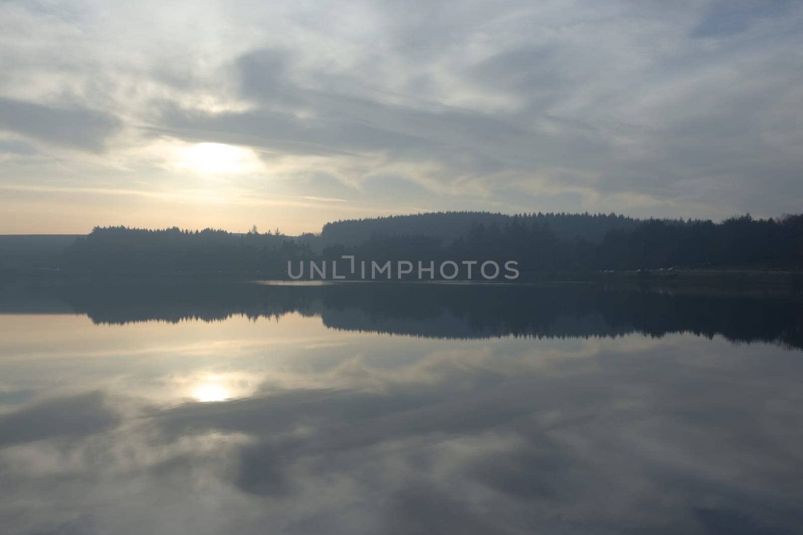 Wide angle symmetrical water reflection landscape during winter at redmires reservoirs near sheffield. Striking cloudscape and forest line reflected