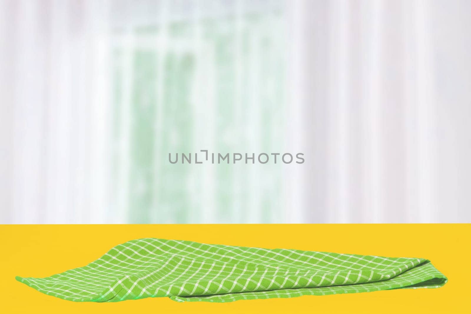 Empty table product. Closeup of a empty green checkered tablecloth or napkin on a yellow table over abstract blurred curtain background. Template for your food and product display montage.