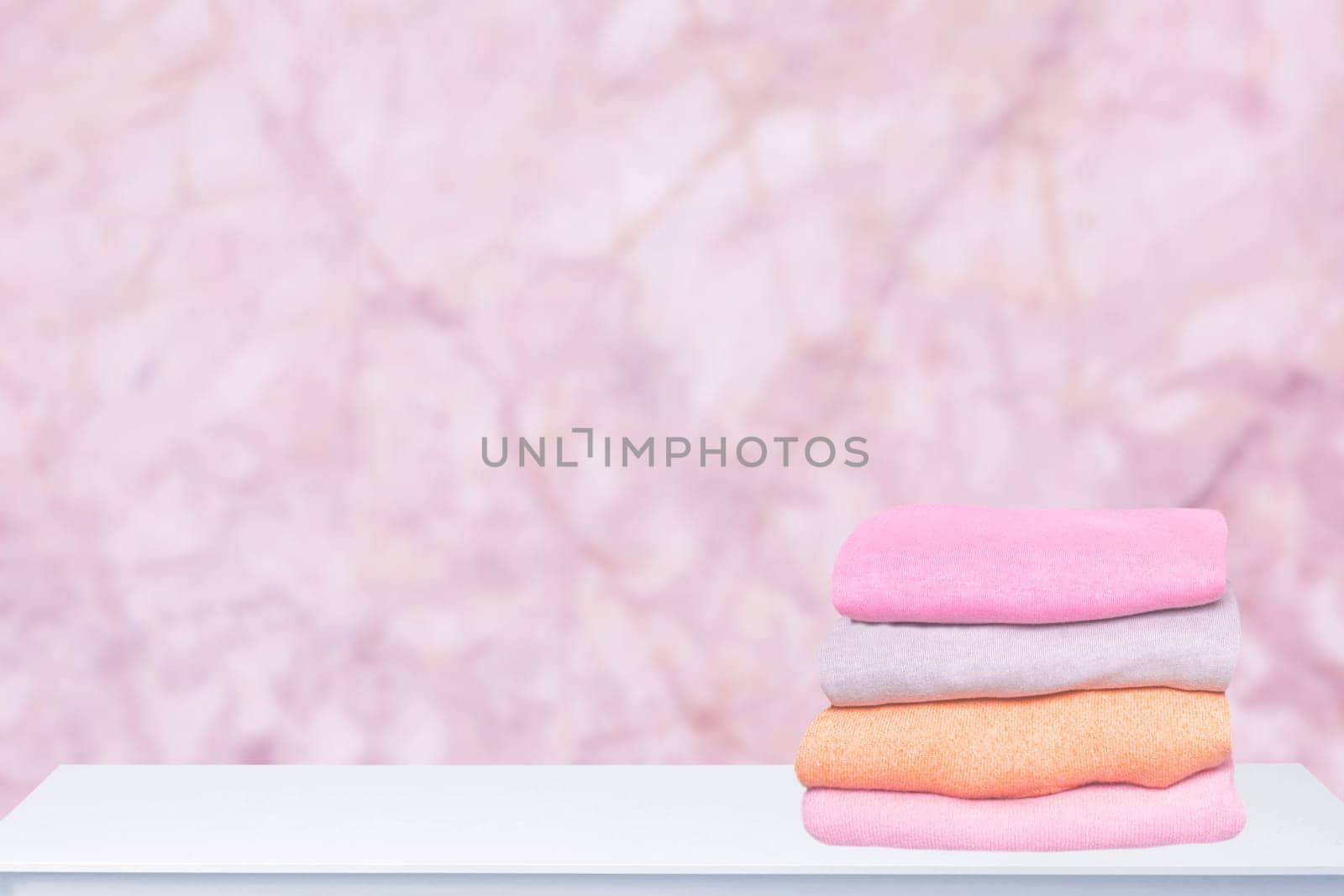 A pile of colorful cozy warm sweaters on a bright table against abstract blurred pink background. Autumn and spring clothes. Space for product display montage.
