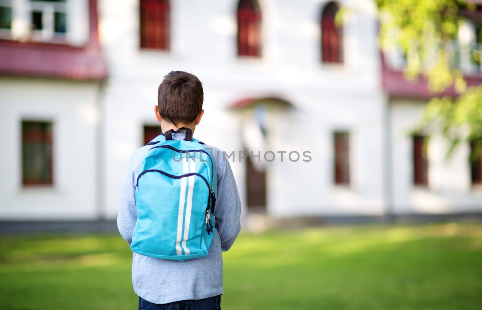 Boy with rucksack infront of a school building. Child with a backpack