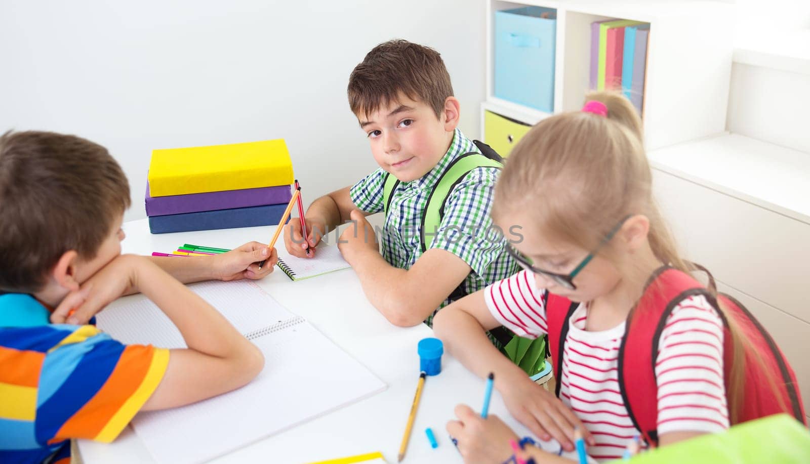 Children sitting in the room with books. Pupils writing at school