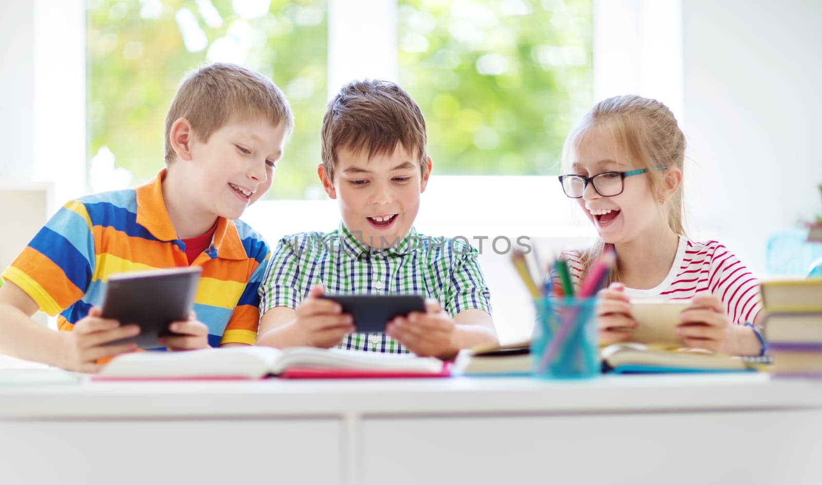 Children sitting in the room with smart phones. Pupils surfing at school