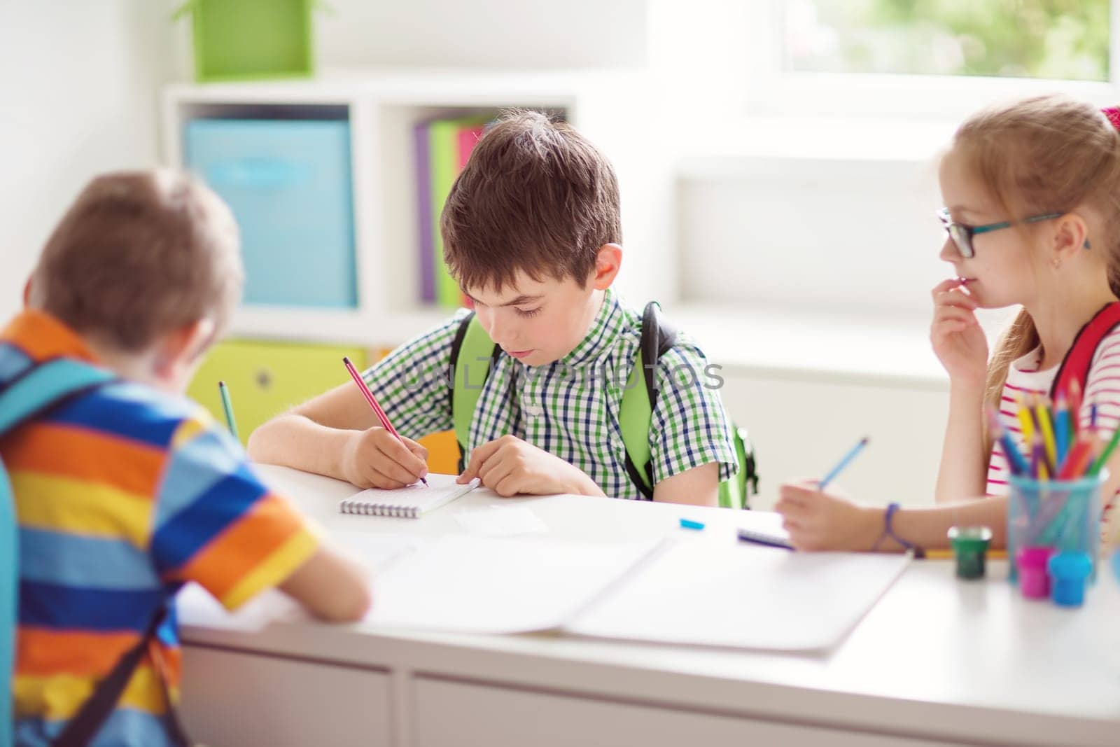 Children sitting in the room with books. Pupils writing at school