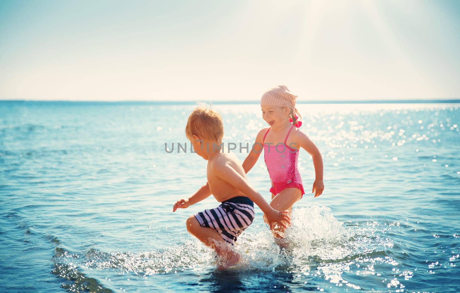 Boy and girl playing on the beach on summer holidays. Children in nature with beautiful sea, sand and blue sky. Happy kids on vacations at seaside running in the water