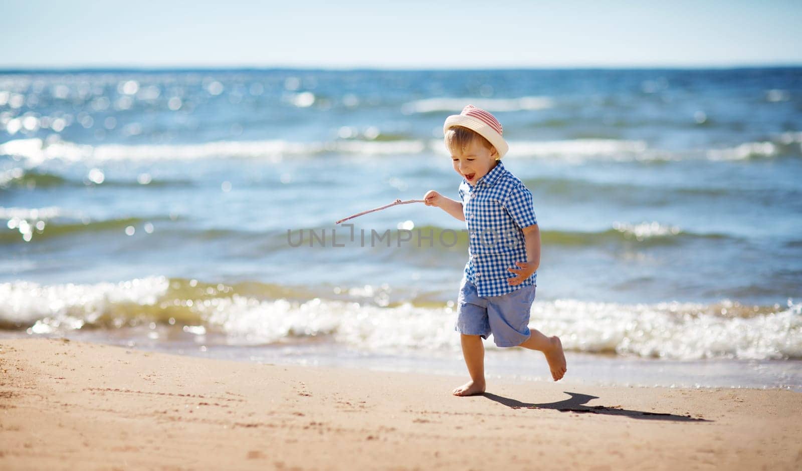 Boy walking at sea in straw hat. Child on vacation in summer at the beach