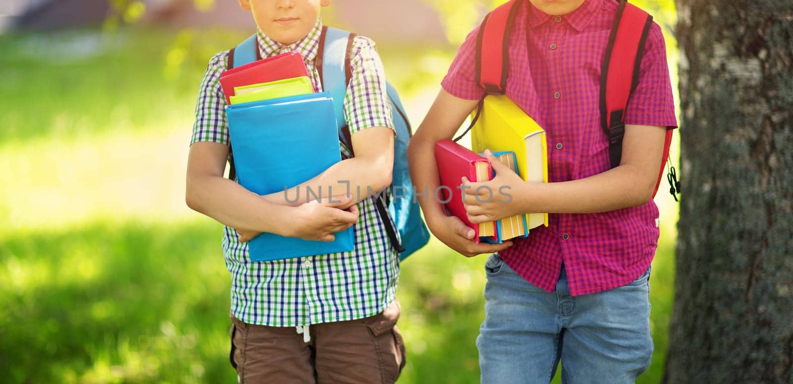 Children with rucksacks standing in the park near school. Pupils with books and backpacks outdoors