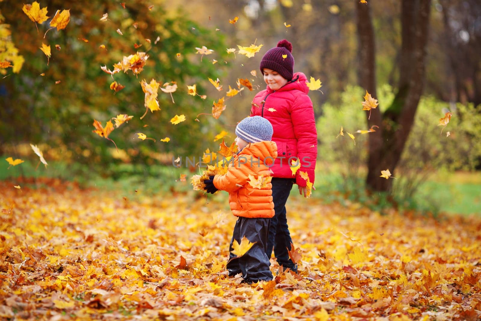 children throwing leaves in beautiful autumnal day. Boys playing outdoors in the park