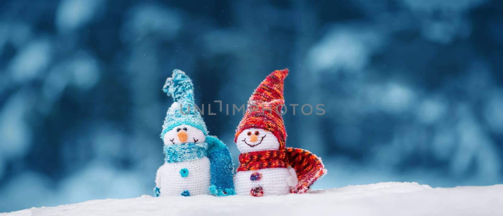 little knitted snowmans on soft snow on blue background