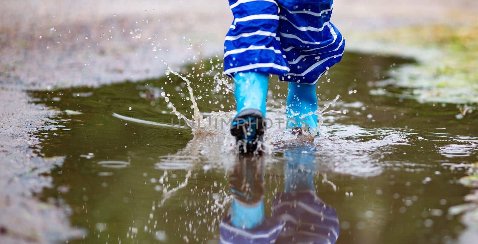 Child walking in wellies in puddle on rainy weather. Boy under rain in summer