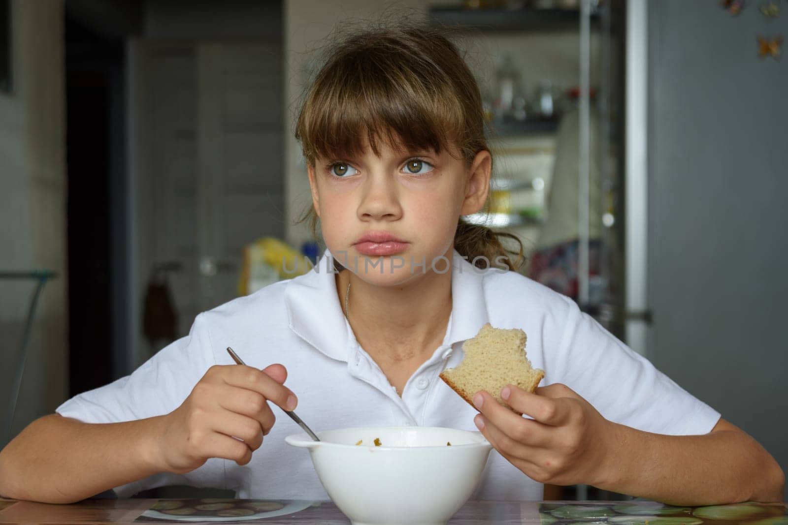 Girl thoughtfully eats soup at the table in the kitchen