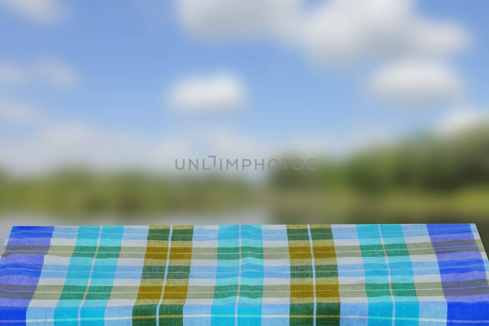 Empty table product. Empty wooden deck table covered with a blue checkered tablecloth over abstract blurred natural backdrop. Space for your food and product display montage.