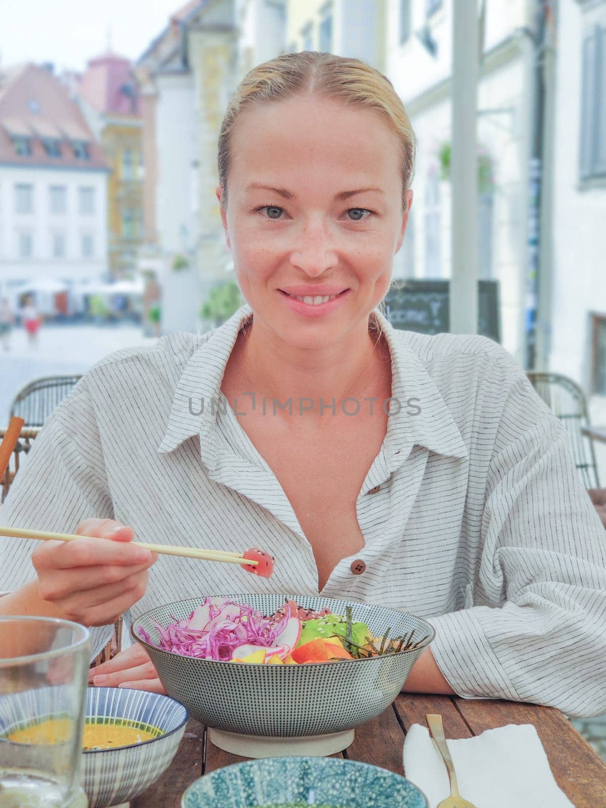 Woman eating tasty colorful healthy natural organic vegetarian Hawaiian poke bowl using asian chopsticks on rustic wooden table. Healthy natural organic eating concept.