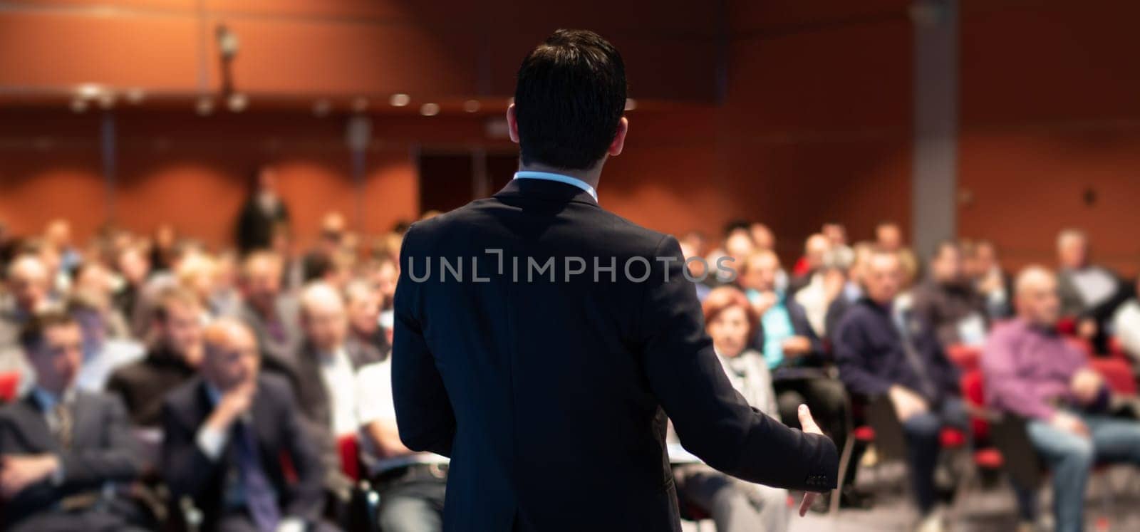 Speaker giving a talk on corporate business conference. Unrecognizable people in audience at conference hall. Business and Entrepreneurship event.