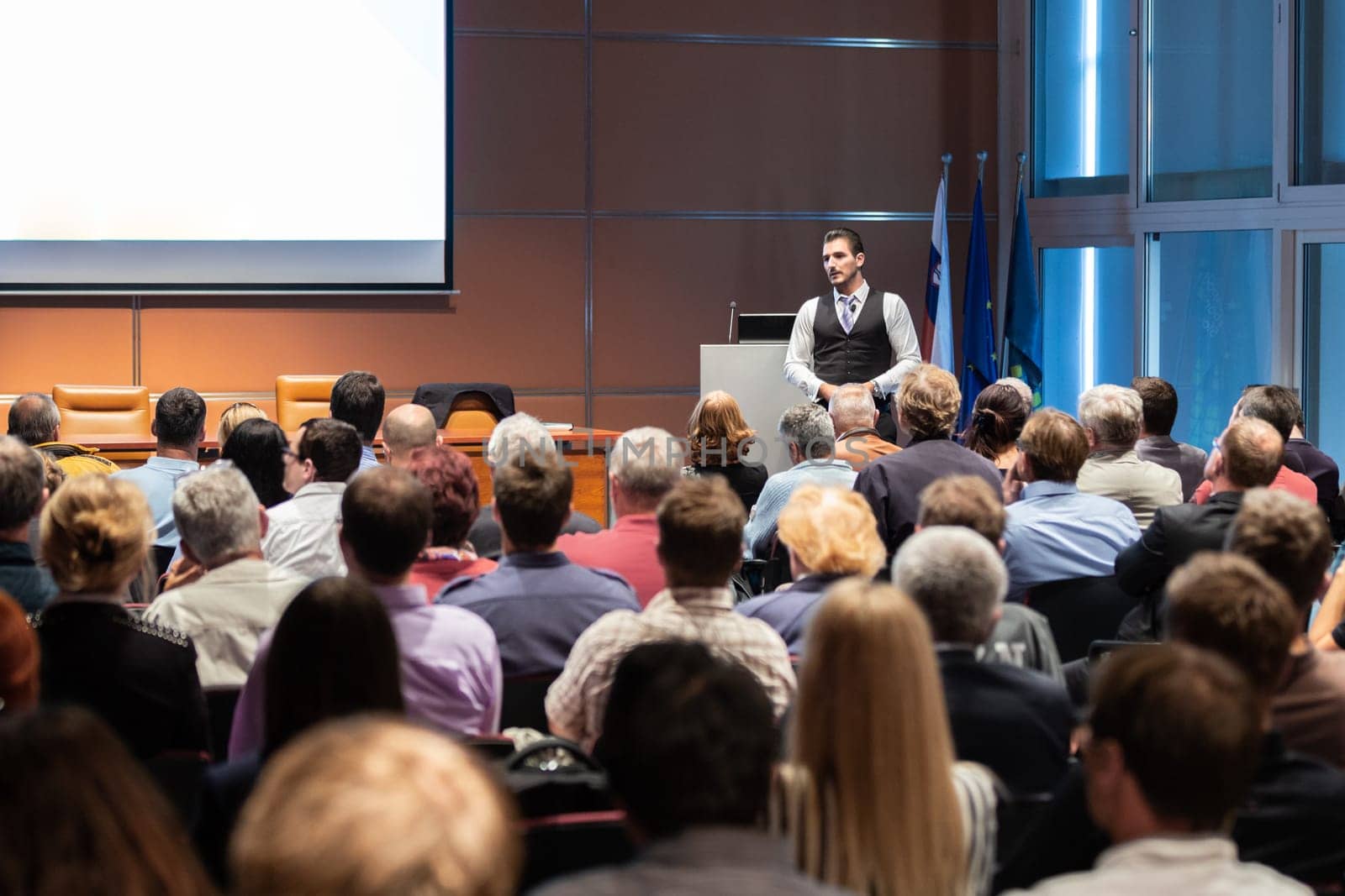 Speaker giving a talk in conference hall at business meeting event. Rear view of unrecognizable people in audience at the conference hall. Business and entrepreneurship concept.