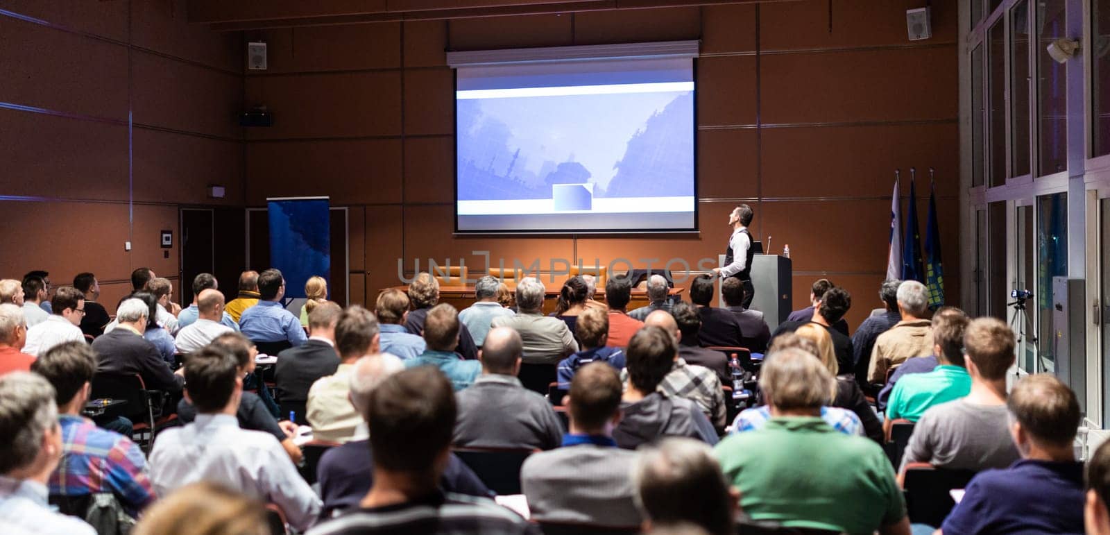 Speaker giving a talk in conference hall at business meeting event. Rear view of unrecognizable people in audience at the conference hall. Business and entrepreneurship concept.