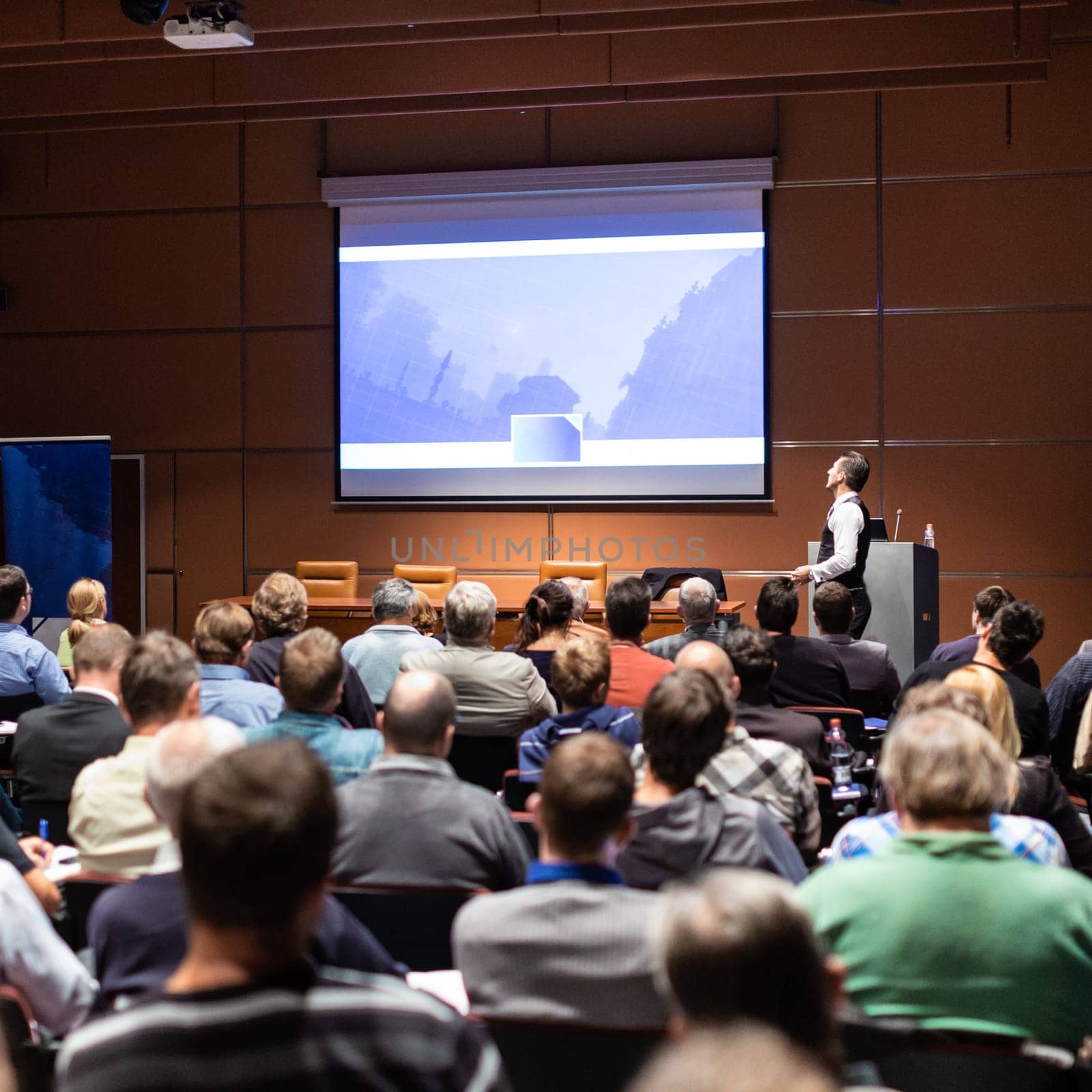 Speaker giving a talk in conference hall at business meeting event. Rear view of unrecognizable people in audience at the conference hall. Business and entrepreneurship concept.