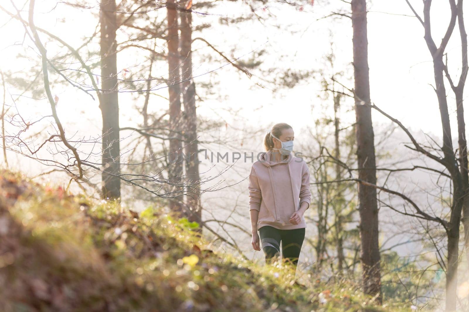 Portrait of caucasian sporty woman wearing a medical protection face mask while walking in the forest. Corona virus, or Covid-19, is spreading all over the world.