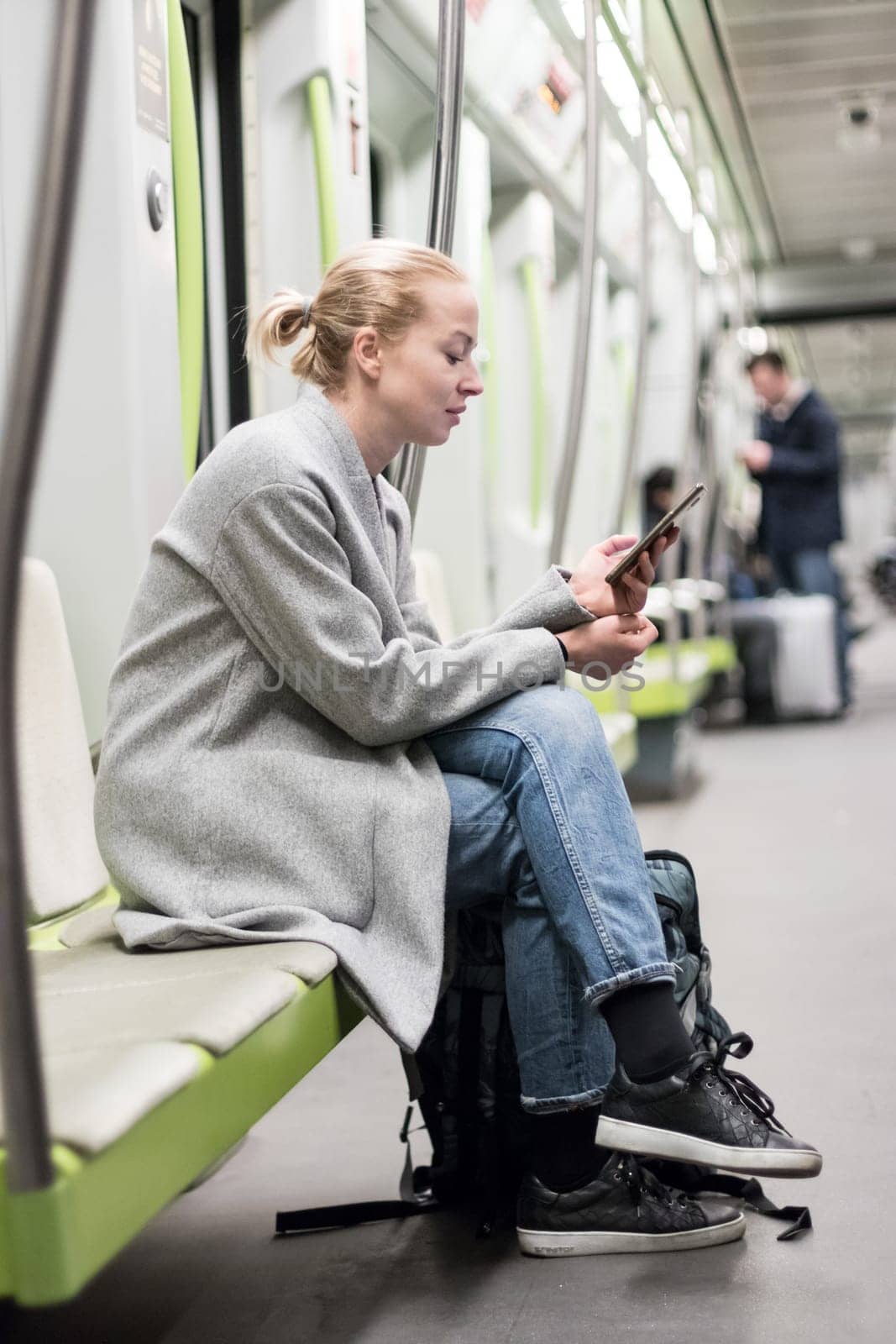 Portrait of lovely girl typing message on mobile phone in almost empty public subway train. Staying at home and social distancing recomented due to corona virus pandemic outbreak.