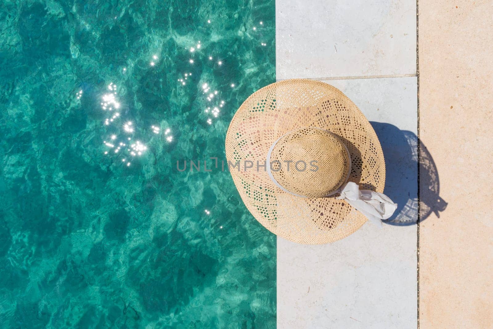 Graphic image of top down view of woman wearing big summer sun hat relaxing on pier by clear turquoise sea.