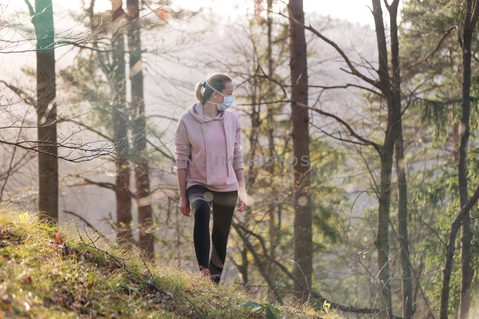 Portrait of caucasian sporty woman wearing a medical protection face mask while walking in the forest. Corona virus, or Covid-19, is spreading all over the world.