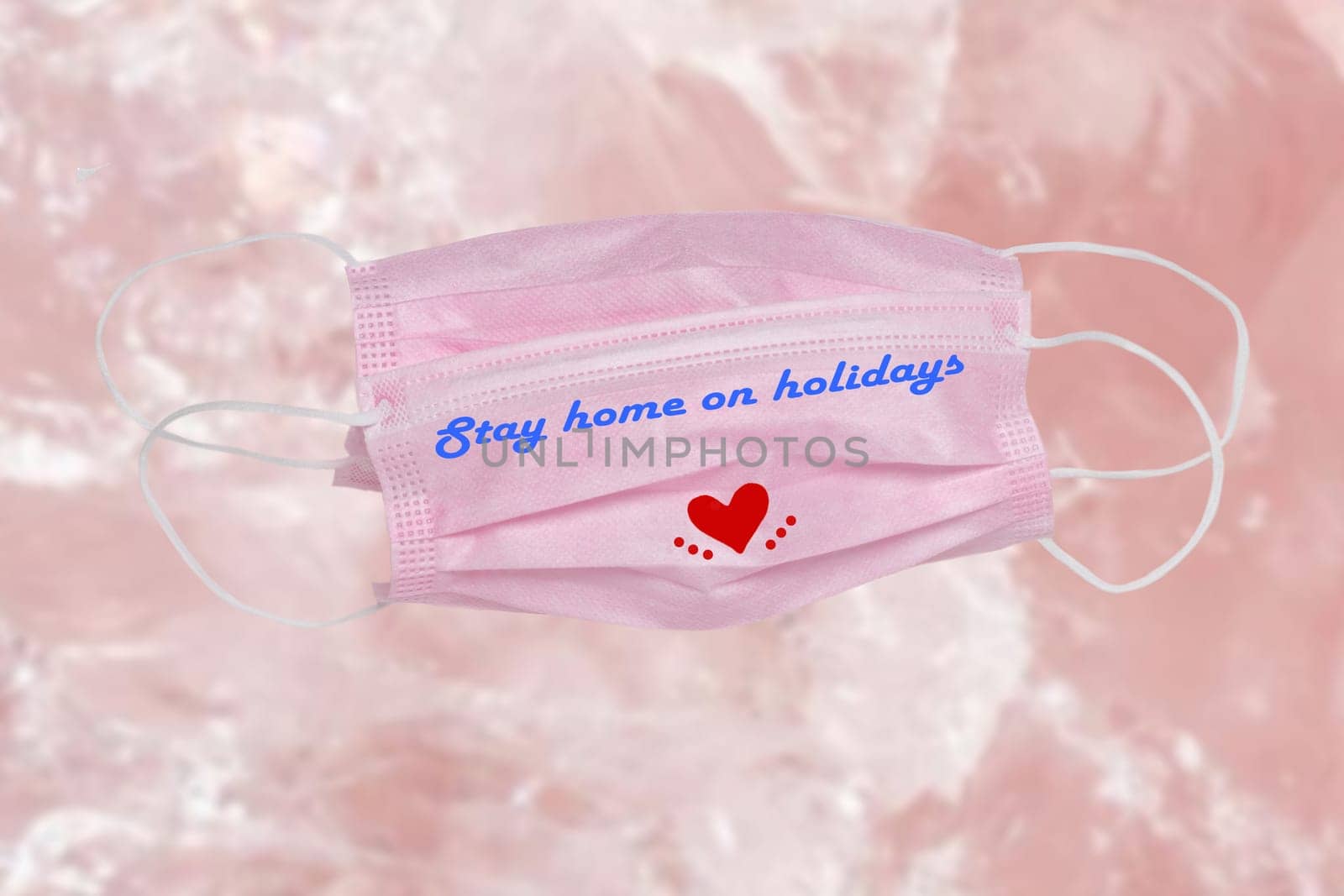 Closeup of two pink surgical masks for protection from covid-19 virus with the inscription stay home on holidays and a red heart on abstract bright background. Pandemic prevention.