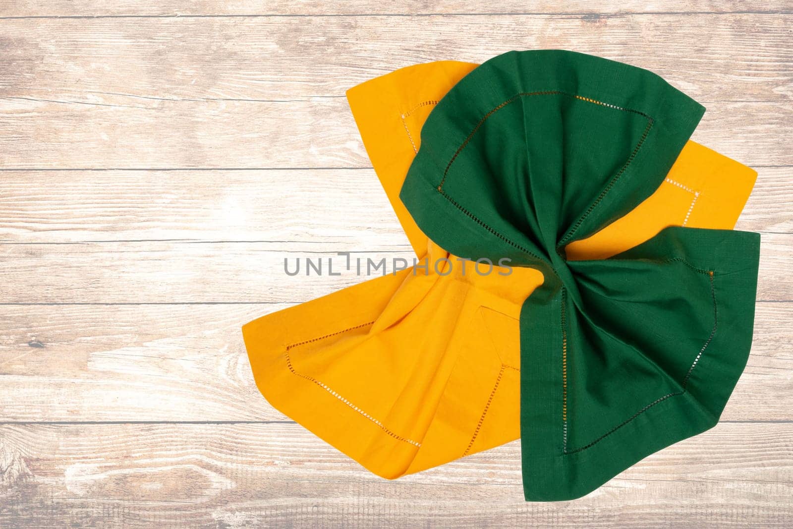 Top view of a folded yellow and green kitchen cloth, textile, tablecloth or napkin on blurred wooden background. Template for your food and product display montage.