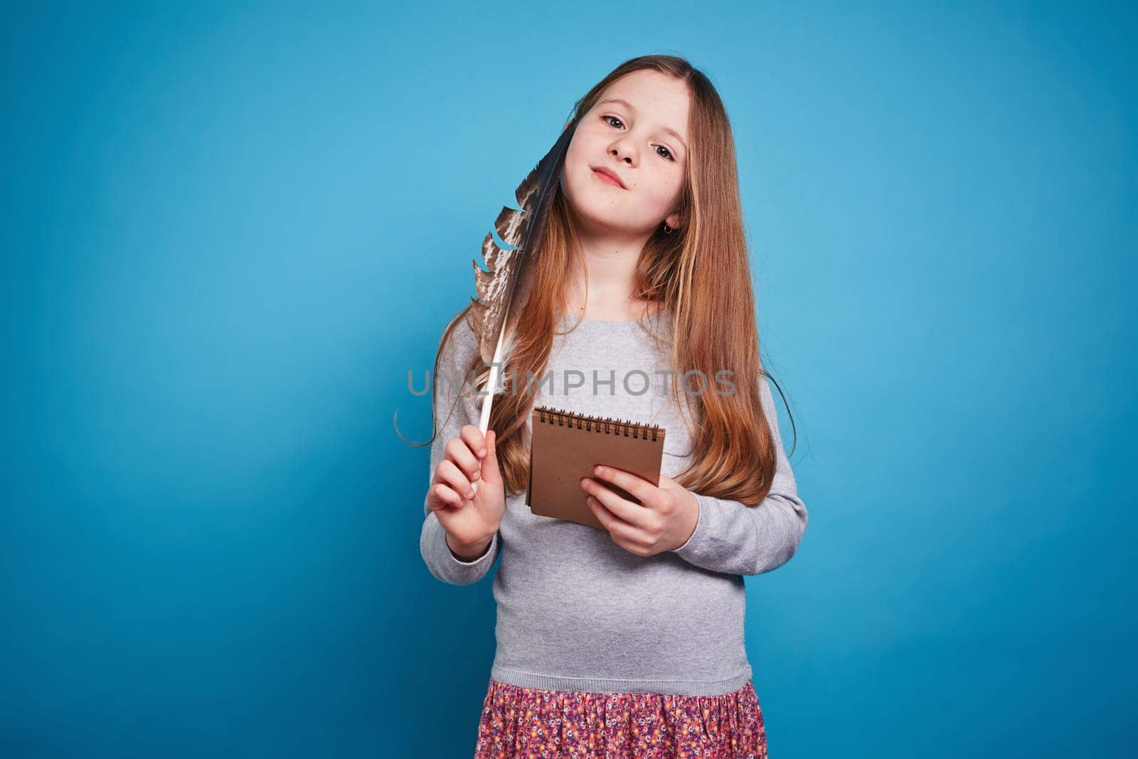 Girl with thoughtful face looking at camera and holding feather pen and notebook in her hands