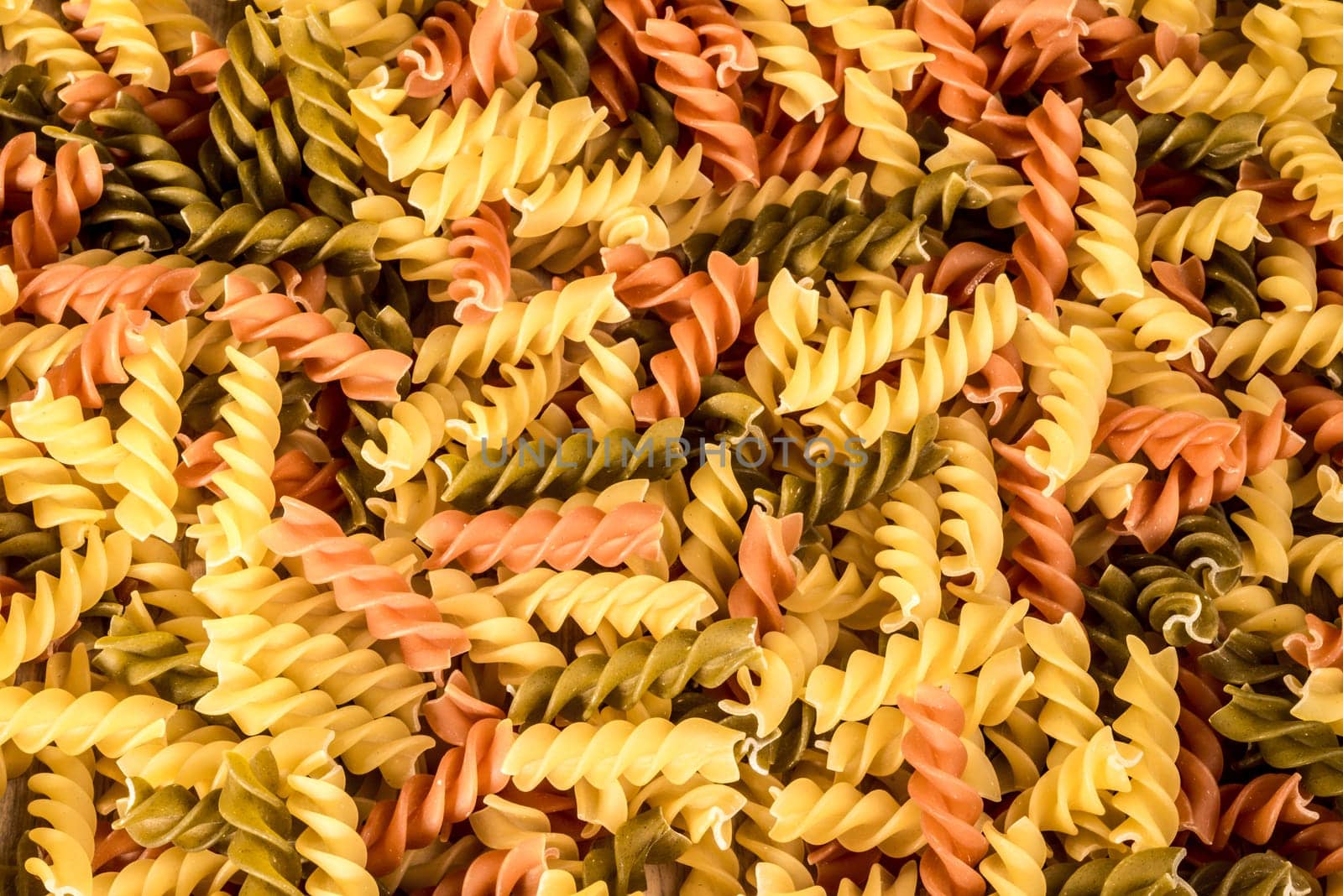 Background image of three different colours of fussili pasta.