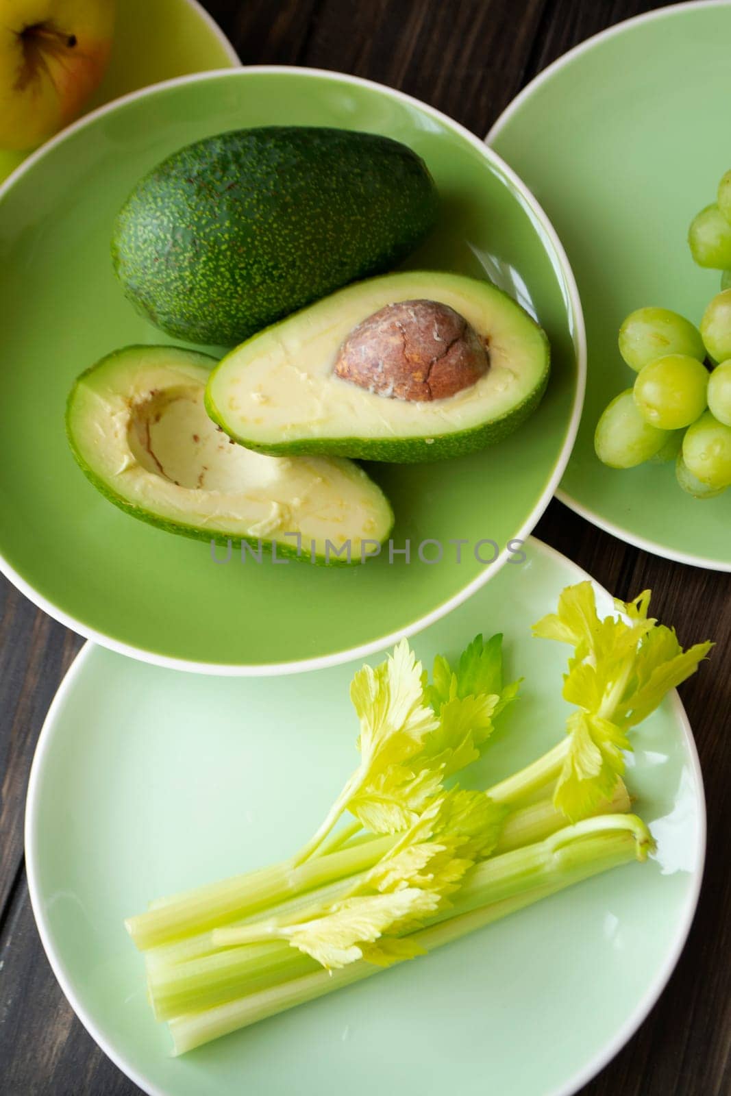 Healthy eating vegan produce. Green vegetables and fruits on green plates. Avocado, green apples, grapes and celery. Vertical image