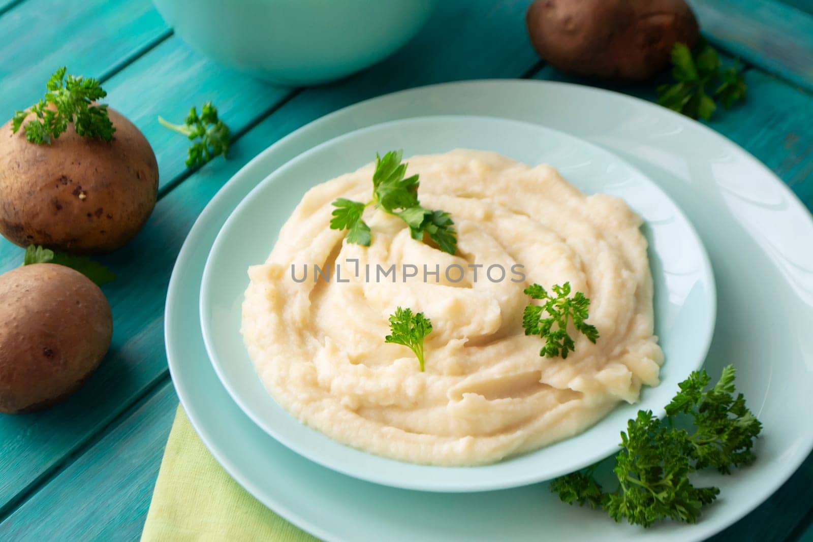 Delicious mashed potatoes with green parsley in a turquoise bowl with vegetables.