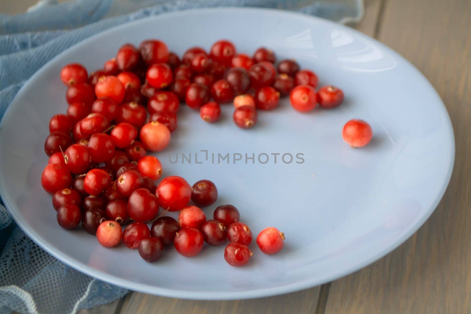 blue plate of cowberries on old wooden table, close up
