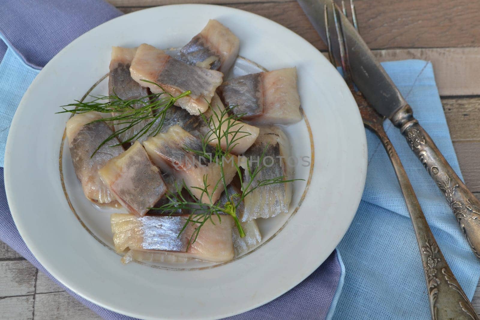 Pieces of herring with onions and dill on old plate in russian style close up