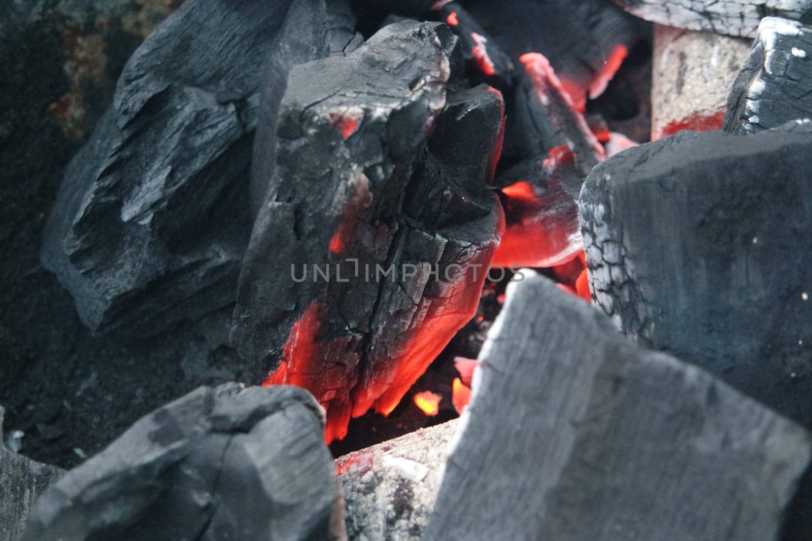 Fire on logs in fire pot with embers and burning coal. Bonfire with blazing red and orange fire flames. Fire background with woods and planks on fire at night view.