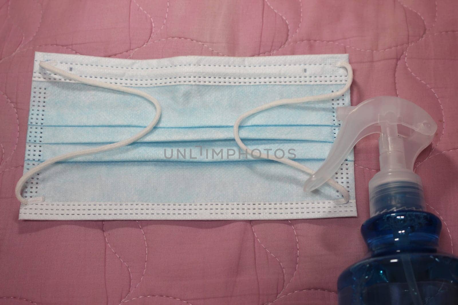blue color cloth face mask with hand sanitizer bottle isolated on pink background