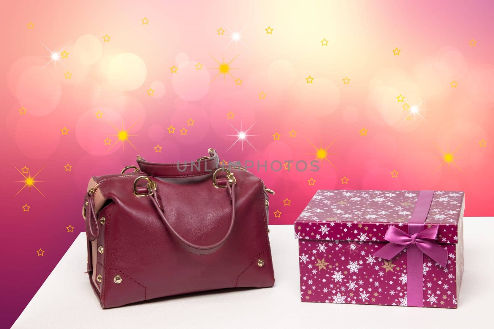 Template for christmas sale. Luxury and stylish womens leather handbag and a gift box on table against abstract festive background . Advertising fashionable woman accessories.