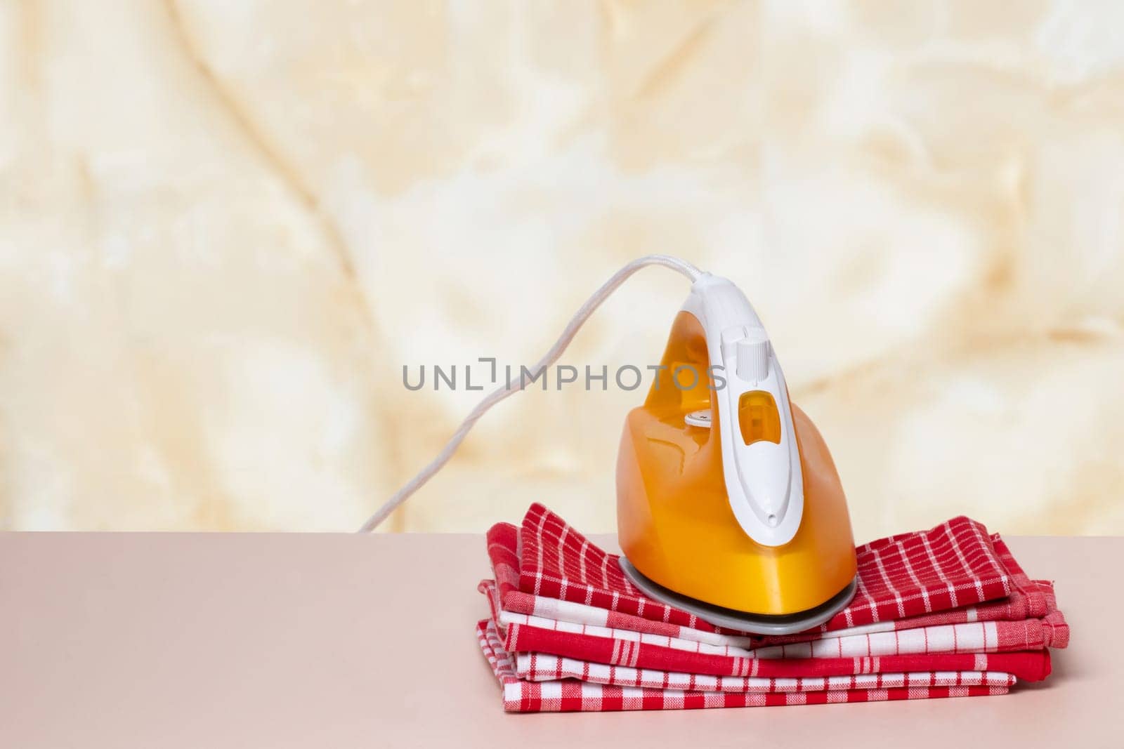 Closeup of a yellow iron on a stack red and white checkered towels on table against an abstract bright backgound. Advertising for the laundry service with space for design.