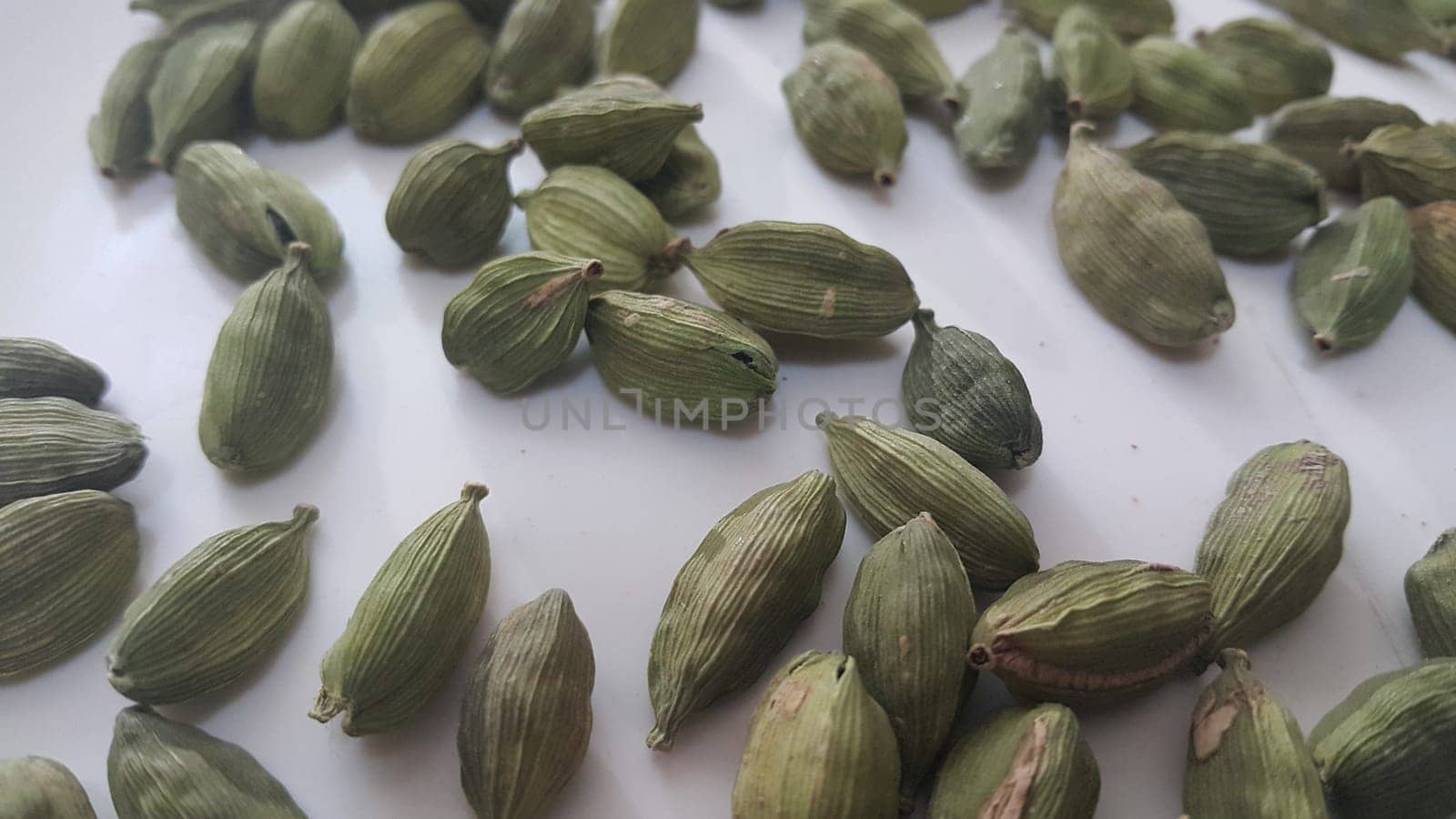 Closeup top view of dried green Elettaria cardamomum fruits with seeds, cardamom spice scattered on a white background