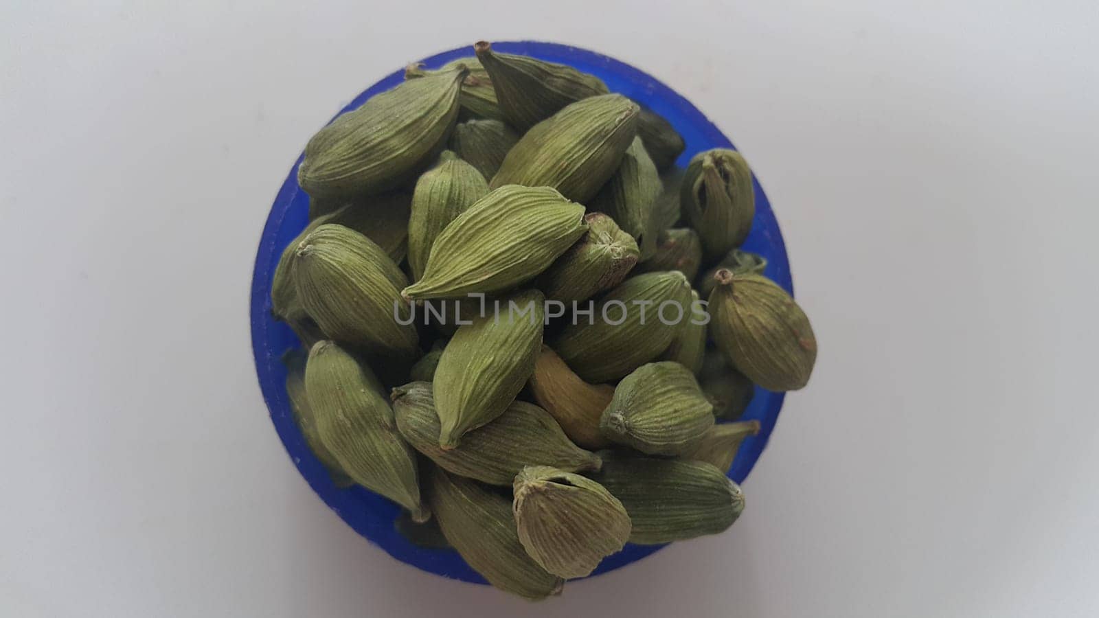Closeup top view of dried green Elettaria cardamomum fruits with seeds, cardamom spice in small bowl on white background