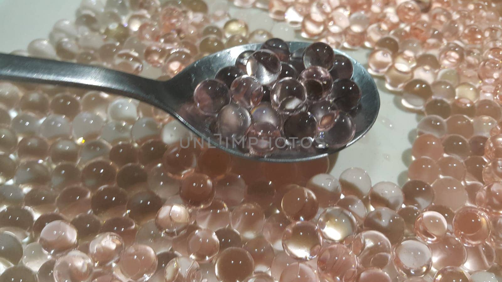 Closeup view with selective focus of shiny glittering orbeez or colorful water balls hydrogel in a silver spoon. Water beads orbeez background.