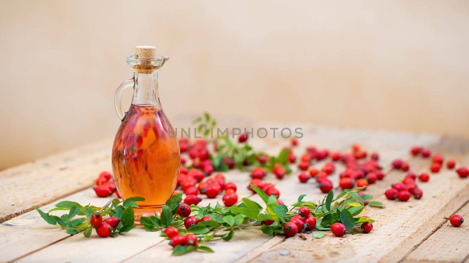 Rosehip oil in bottle laid on wooden palette with copy space. Glass with cork plug full of red oily fluid with berries around. Healthy liquid ingredient on brown desk.